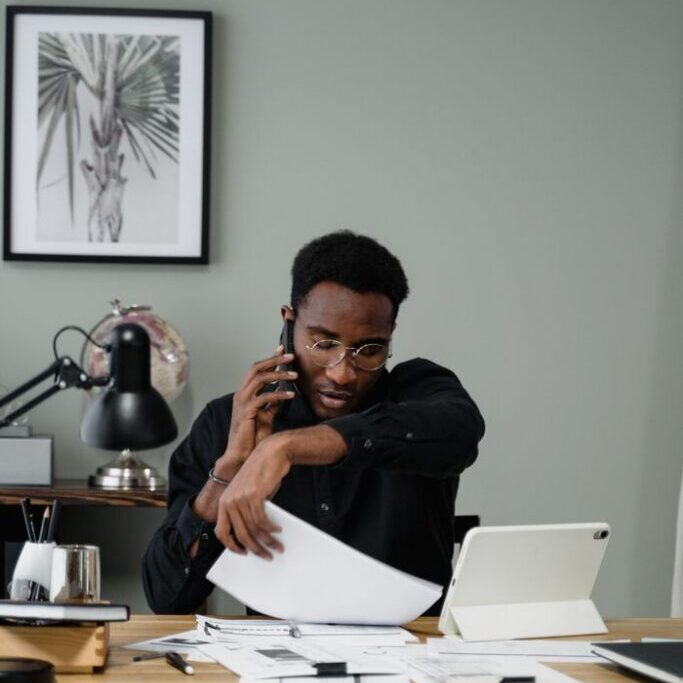 Focused businessman multitasking with smartphone and tablet in modern office setting.